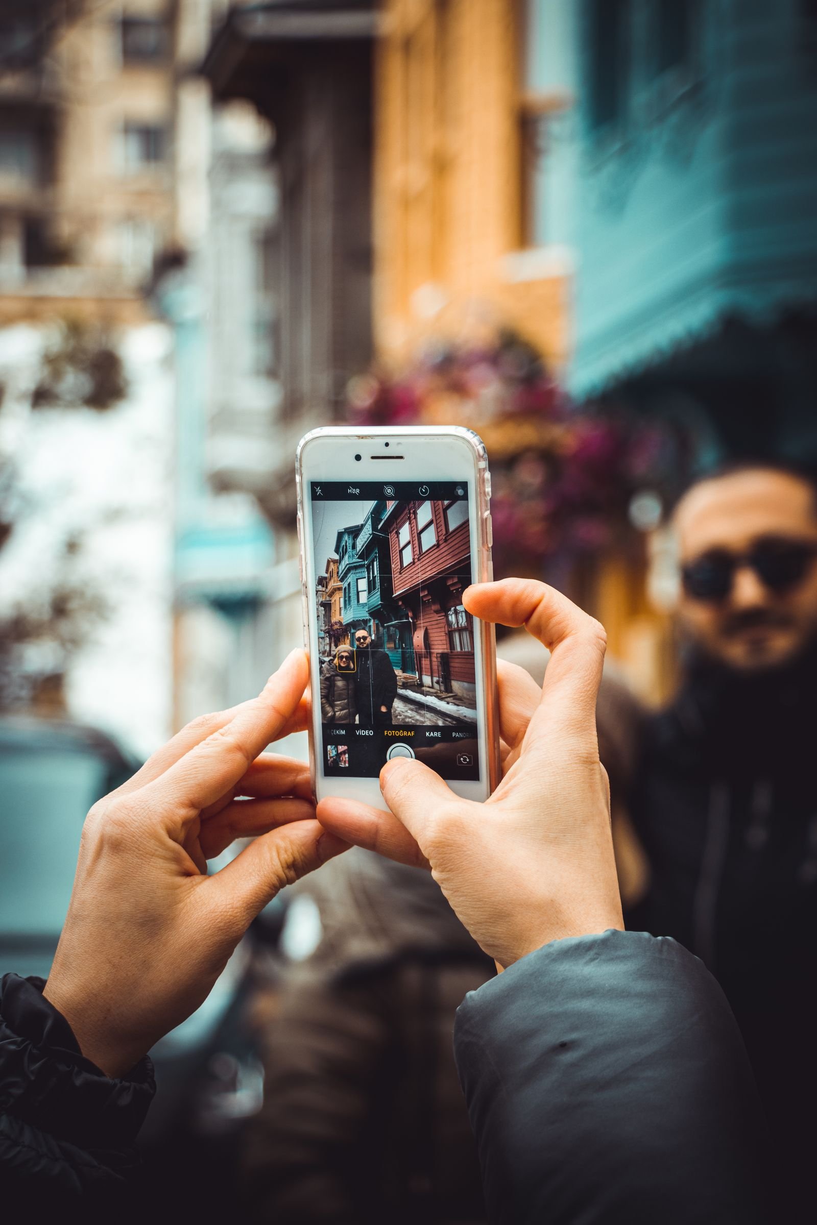 Mãos segurando um smartphone fotografando uma rua colorida, representando a fotografia cotidiana feita por celular