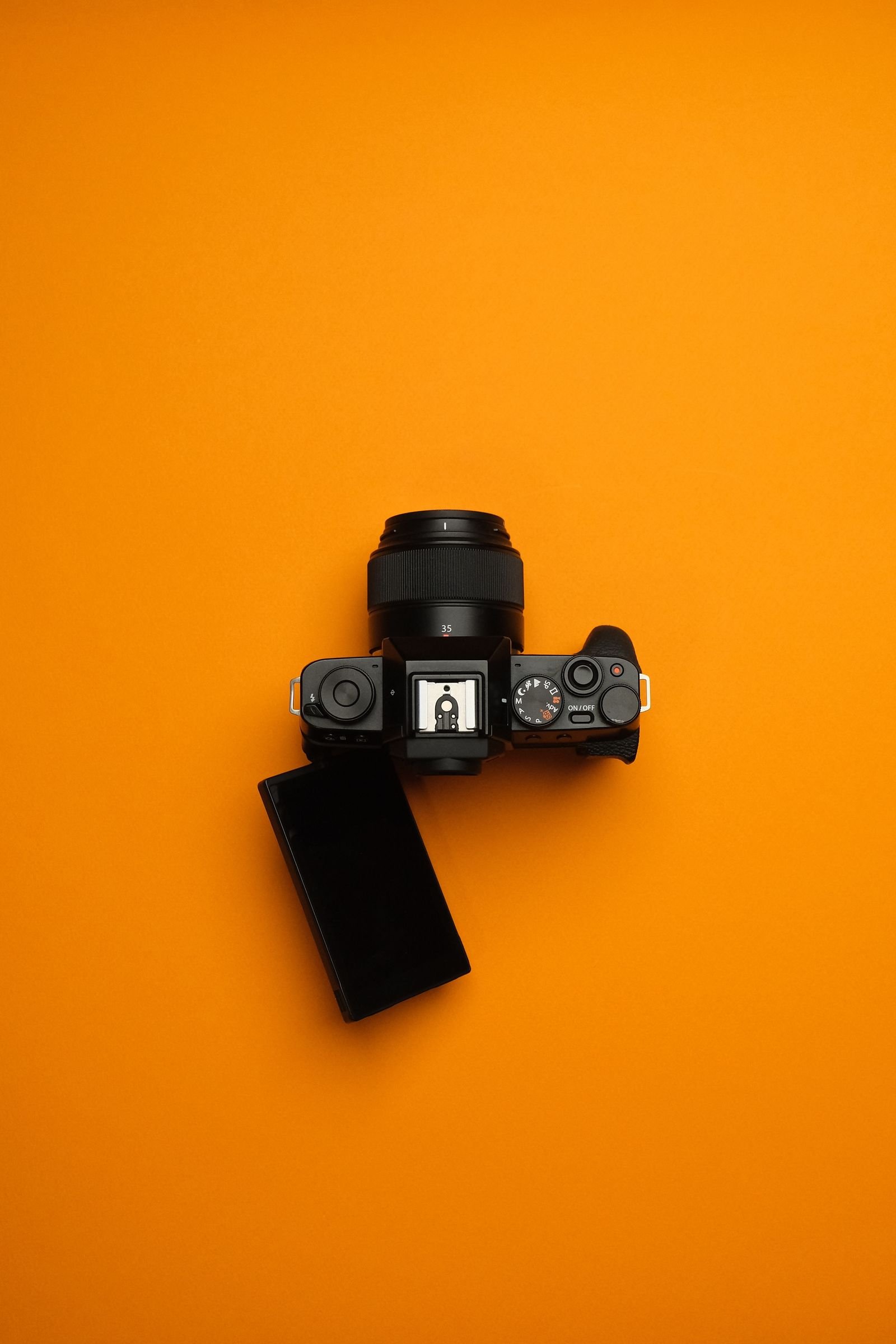 Câmera mirrorless vista de cima sobre fundo laranja, com corpo mais baixo e compacto por não ter o bloco do espelho reflex