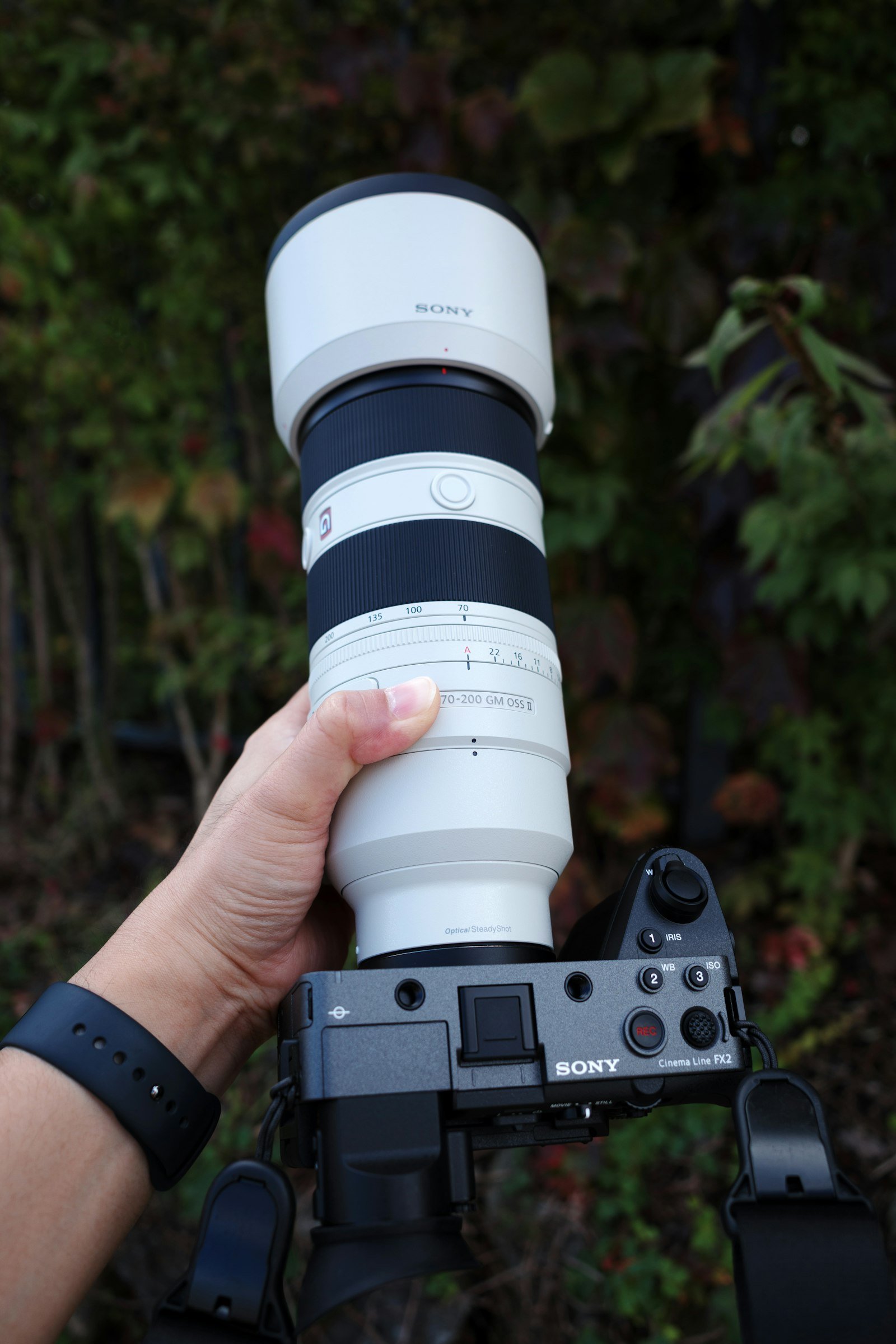 Mão segurando uma câmera mirrorless com lente telefoto profissional 70-200mm, equipamento típico de fotografia esportiva